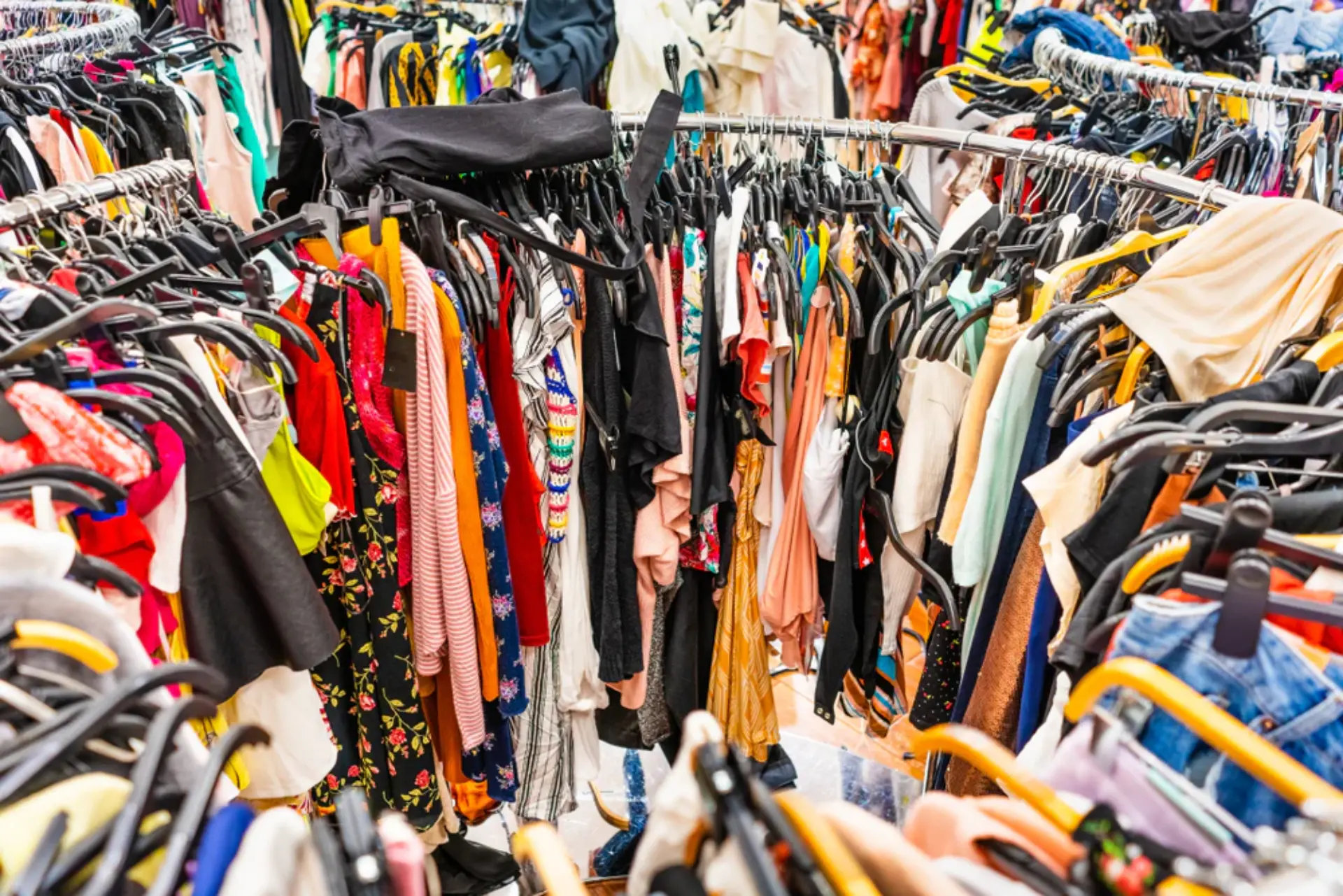 Impacto ambiental de la industria textil y fast fashion Percheros de tienda abarrotados de ropa colgada en perchas, ilustrando el consumo masivo y la industria textil.