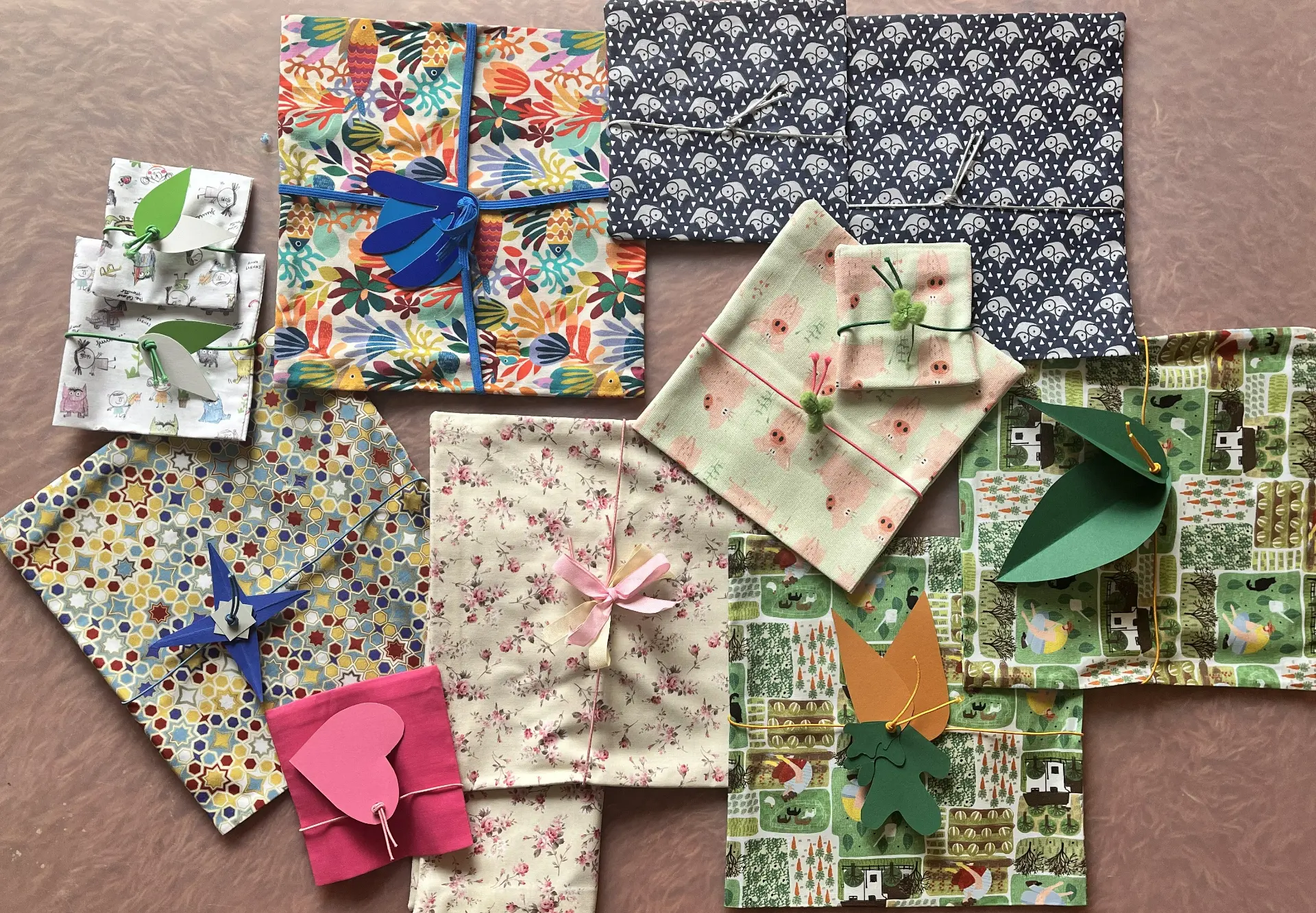 Variedad de envoltorios de tela Furoshiki de colores Variedad de paquetes y regalos de diferentes tamaños envueltos en telas de colores y estampados con lazos y elementos decorativos de papel.