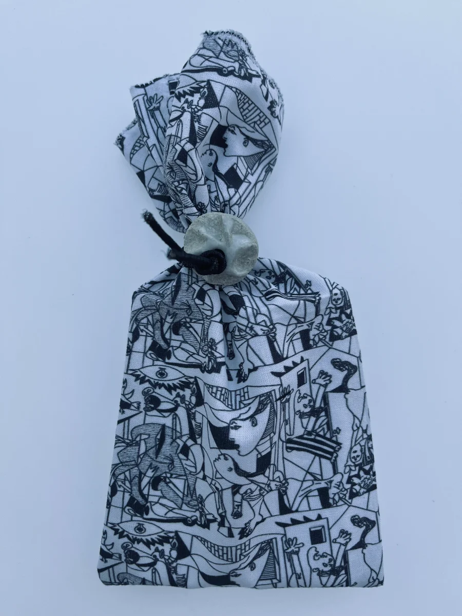 Saquito de regalo confeccionado en tela de algodón estampada con dibujo lineal del Guernica, fruncido arriba con goma y botón de cerámica esmaltada.