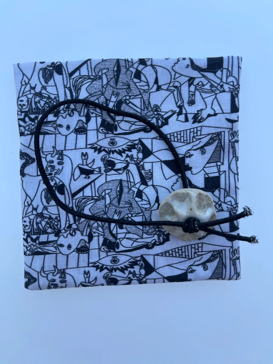 Tela de algodón desplegada con estampado artístico en blanco y negro de Picasso, mostrando la goma elástica negra y la pieza de cerámica esmaltada.