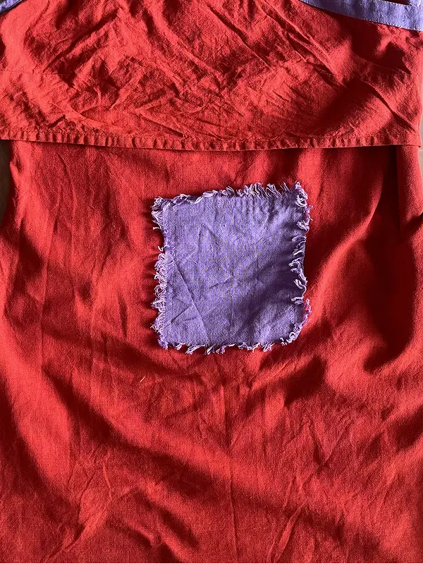 Detalle de costura con retal de tela roja y un parche de tela color lila desgastada cosido en el centro, mostrando la textura del tejido.