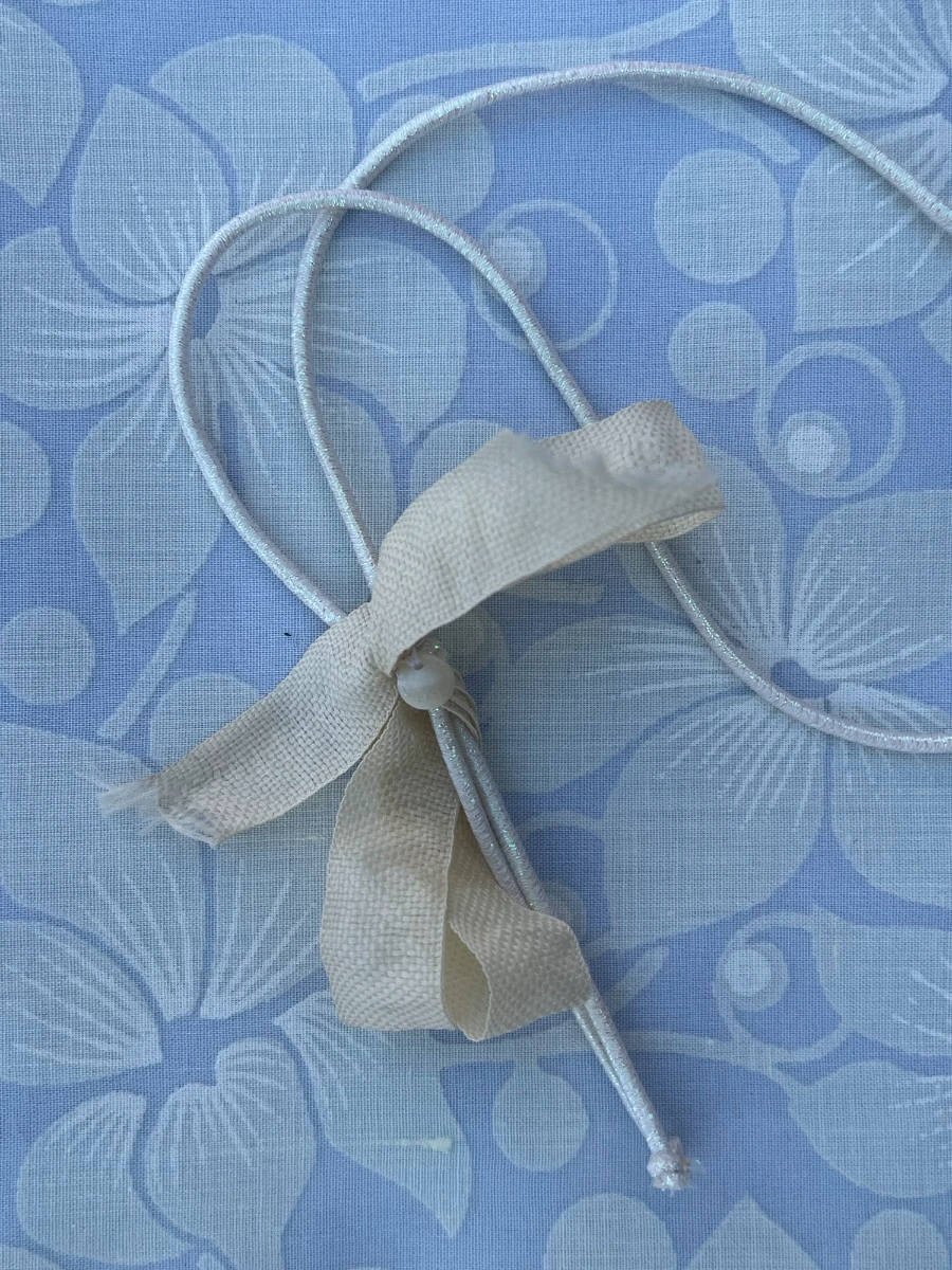 Primer plano de un cordón blanco brillante con un lazo beige de tejido rústico atado sobre la tela azul flora