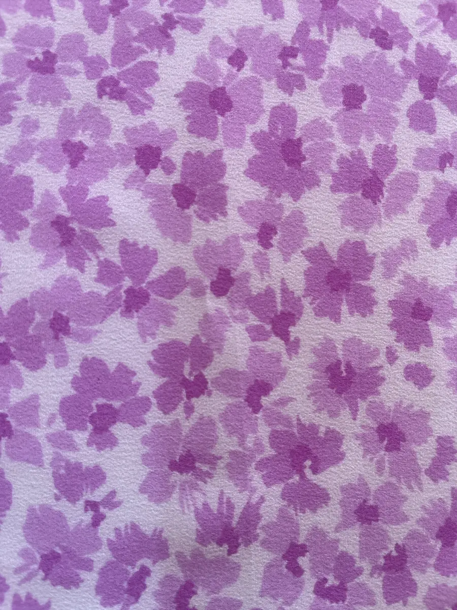 Primer plano de tela de algodón con estampado continuo de pequeñas flores en tonos violeta y lila sobre fondo claro.