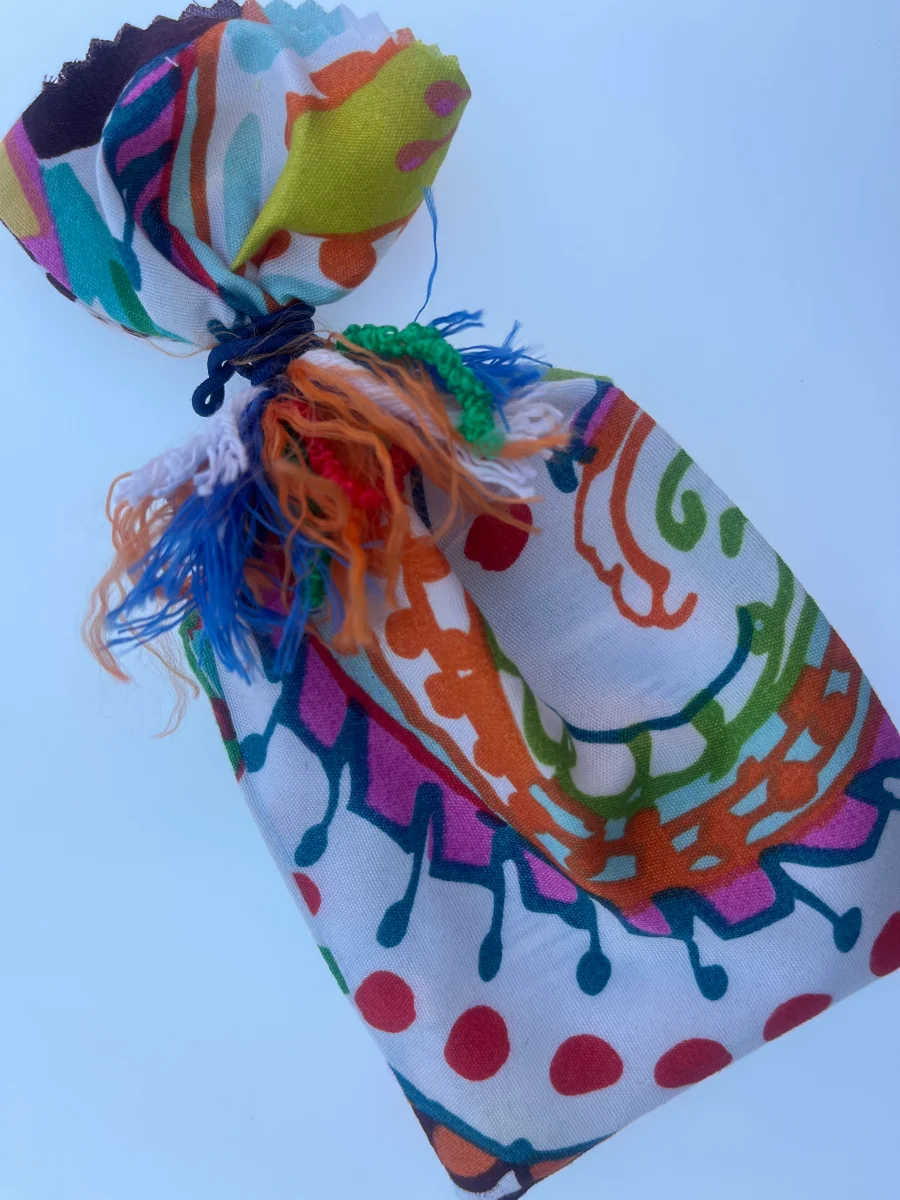 Saquito de regalo hecho de tela estampada multicolor, fruncido y atado en el cuello con una goma azul y flecos sueltos.