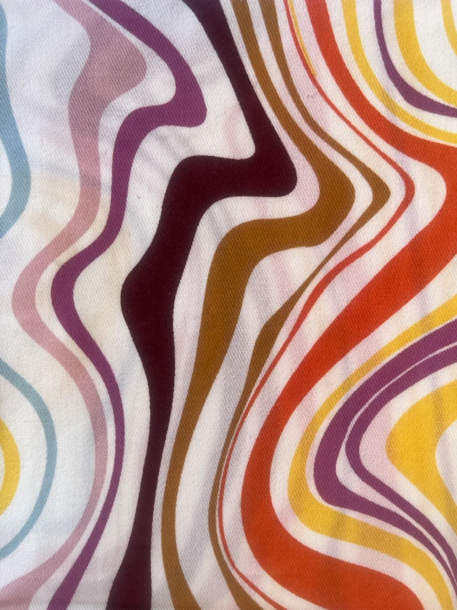 Primer plano de la textura del tejido con estampado de líneas curvas y ondas en tonos granate, ocre, naranja, rosa y azul sobre fondo blanco.