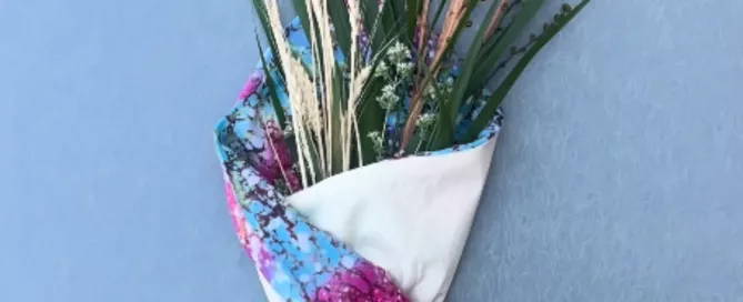 Ramo de espigas, hojas verdes y flores secas envuelto cuidadosamente en una tela artesanal multicolor y atado con un cordón.