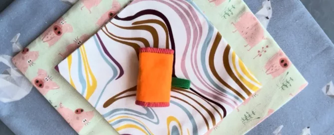 Tres telas estampadas superpuestas con un pequeño rollo o estuche de tela naranja ubicado justo en el centro.