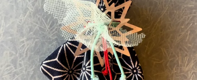Bolsita de tela azul marino con estampado geométrico blanco, cerrada en la parte superior con un adorno de madera en forma de estrella y cordones.