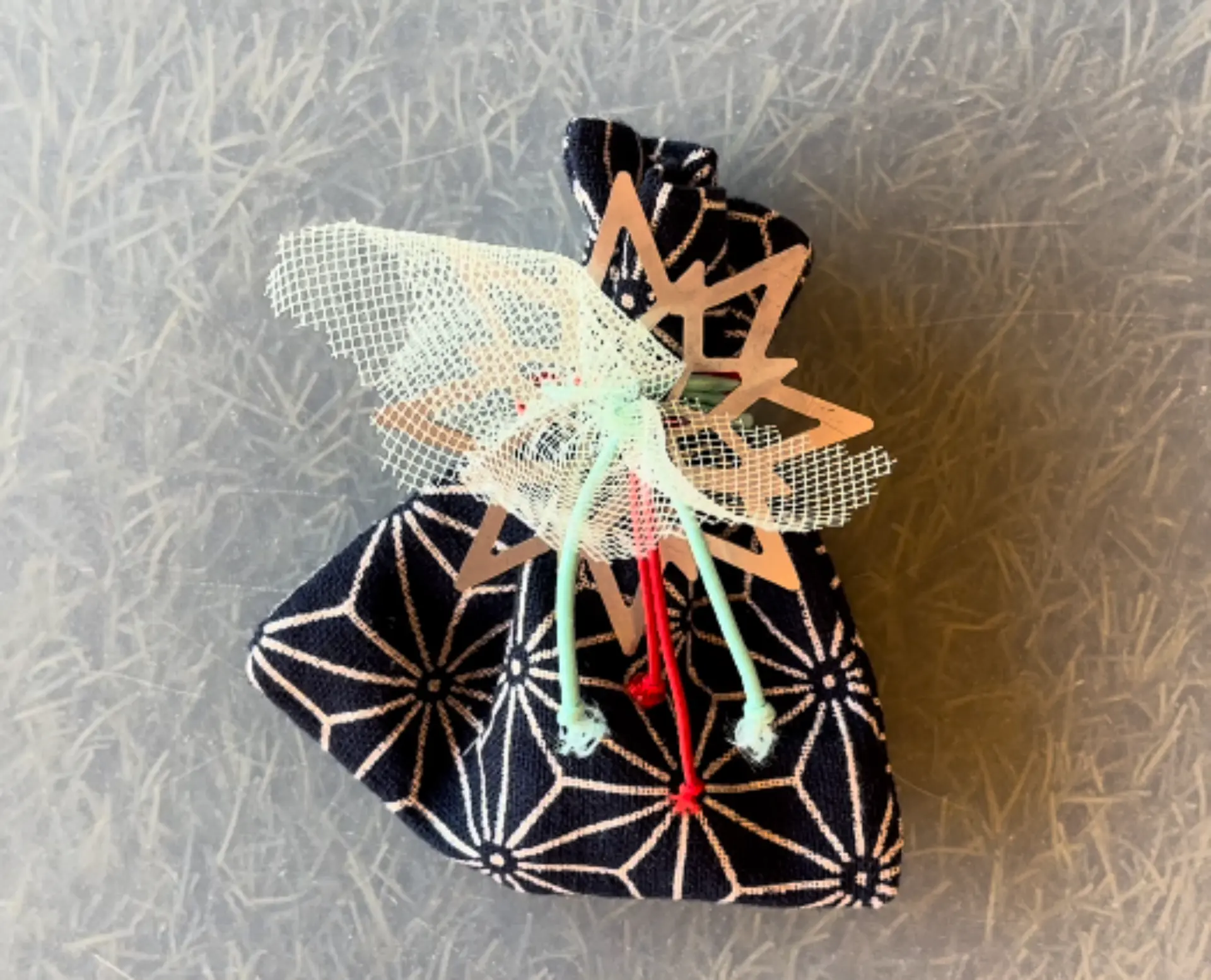 Bolsita de tela azul marino con estampado geométrico blanco, cerrada en la parte superior con un adorno de madera en forma de estrella y cordones.